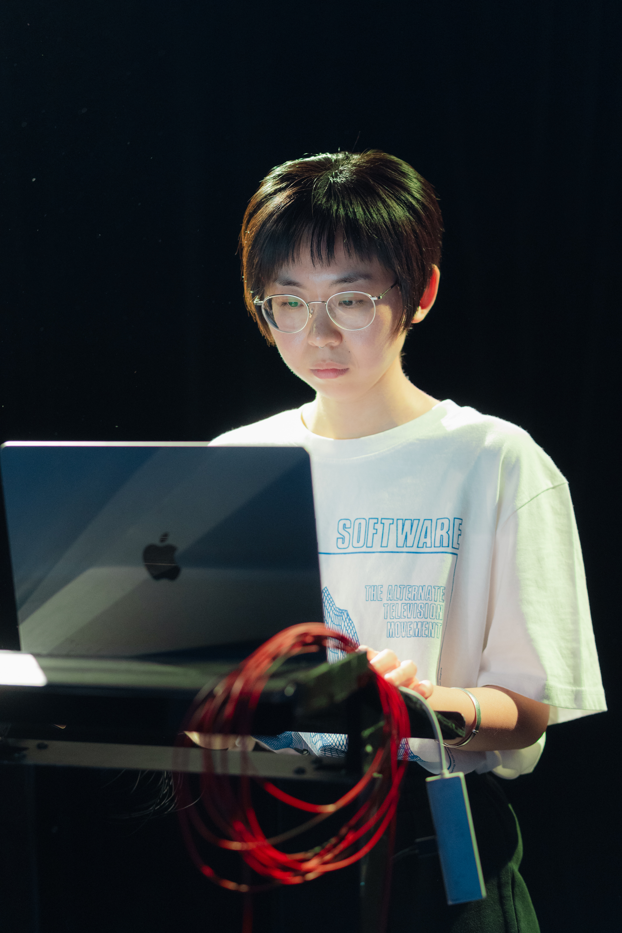 A chinese woman standing behind a macbook air with a roll of red electric wires next to it.