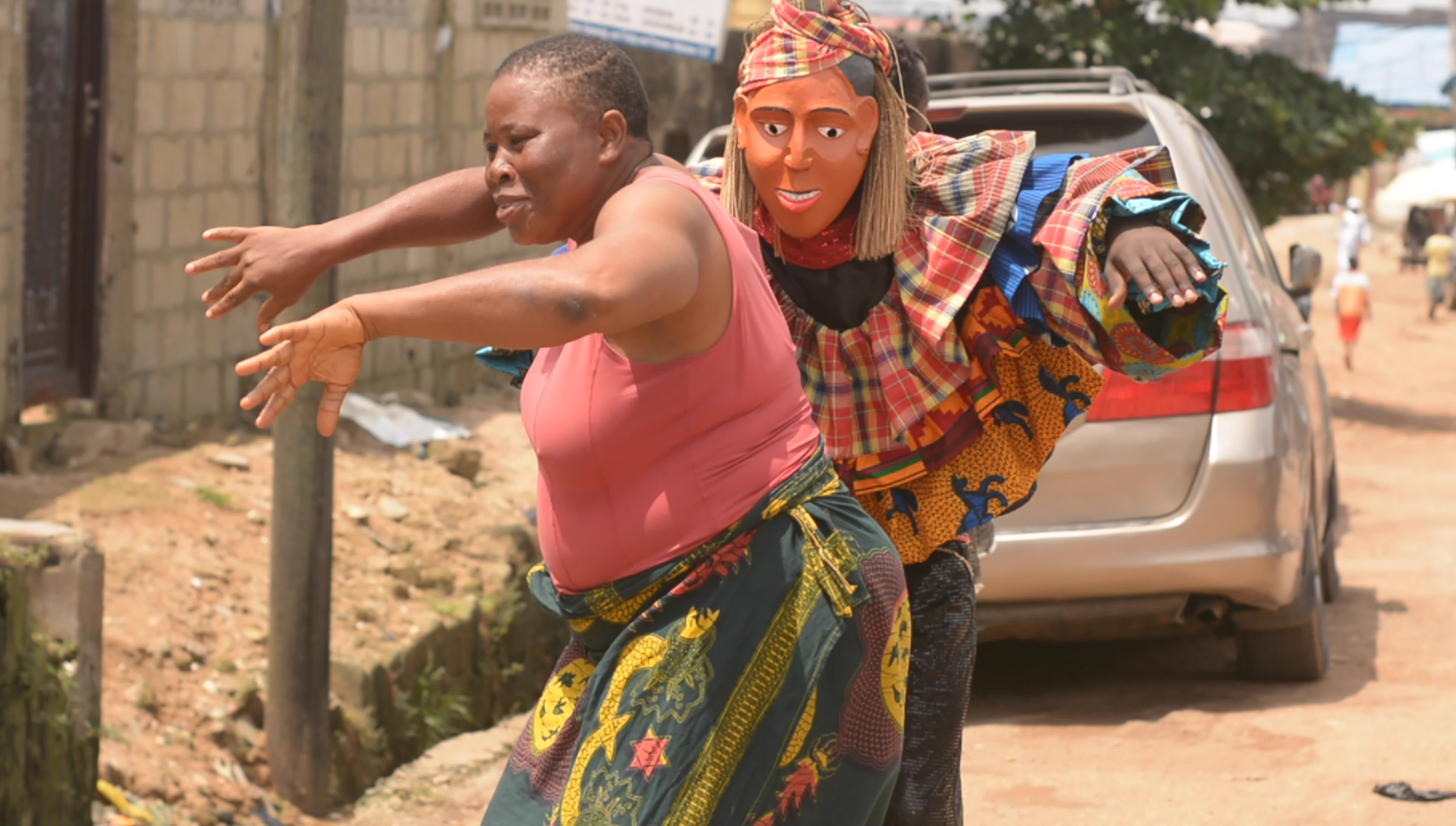 An african woman on the left dancing with a man wearing a masquerade mask on the right behind her